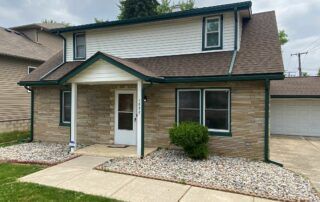 Brick house with a front porch, white door, and gravel landscaping beside a driveway