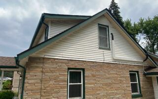 Small house with tan siding and stone facade under a cloudy sky