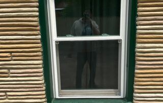 Person reflected in a window on a green-trimmed building with tan siding.