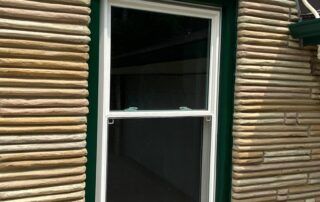 White-framed window in a tan log-sided wall with dark interior behind it