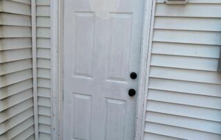 White front door with black handles beside beige vinyl siding