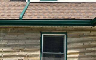 House roof with green gutter and a small window beneath brown shingles