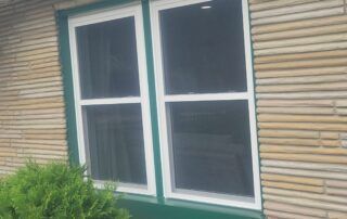 White-framed window with dark curtains on a bamboo wall, with green plants below