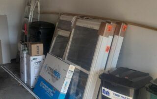 Stacked window frames and boxes in a storage area, leaning against a wall.