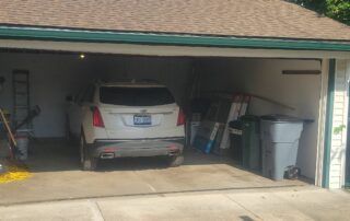 SUV parked in a cluttered garage with boxes and trash bins along the walls