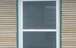 Beige house siding with a white-framed window and closed blinds