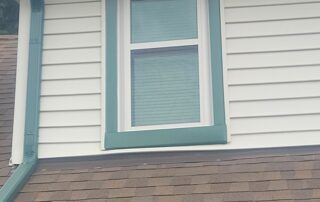 House exterior with white siding, teal-trimmed window, and brown shingled roofline.
