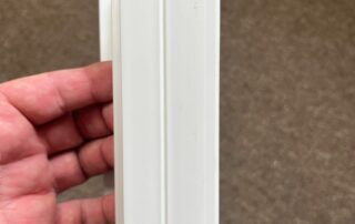 Hand holding a white vertical trim piece against a brown carpeted floor