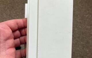 Hand holding a white door or panel against a beige background