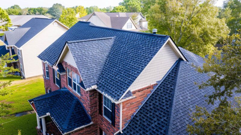 Aerial view of brick houses with dark gray roofs in a green suburban neighborhood