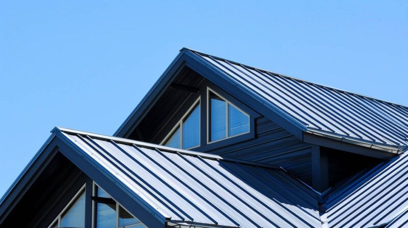 Modern building roof with blue metal panels and dormer windows against a clear sky