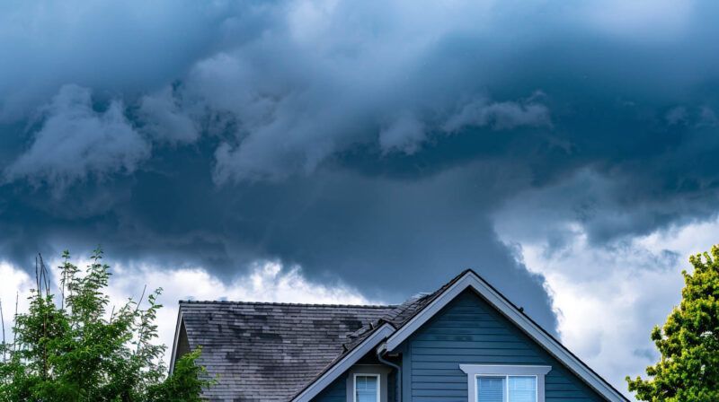 Dark storm clouds over a blue house roof with trees below