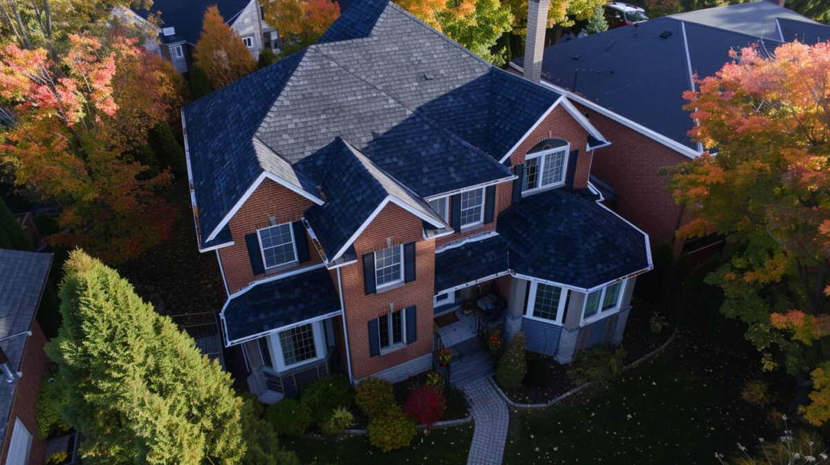Aerial view of a large brick house with dark roof surrounded by colorful autumn trees