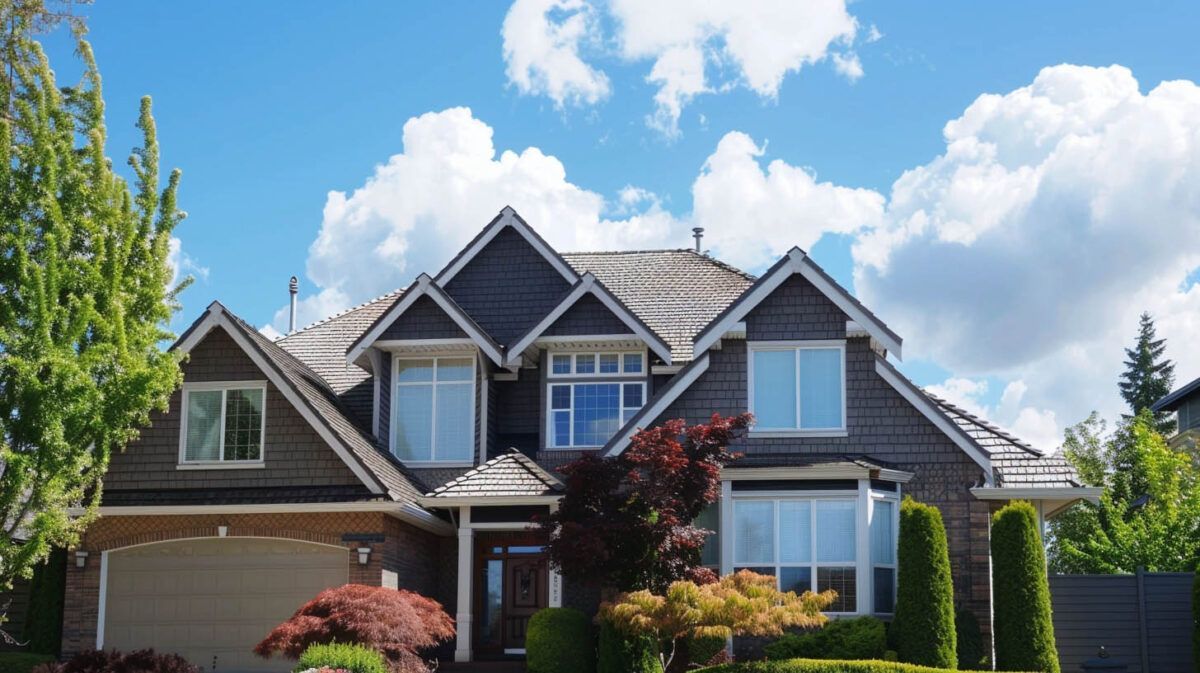 Suburban house with gray siding, gabled roof, and landscaped front yard under a bright blue sky