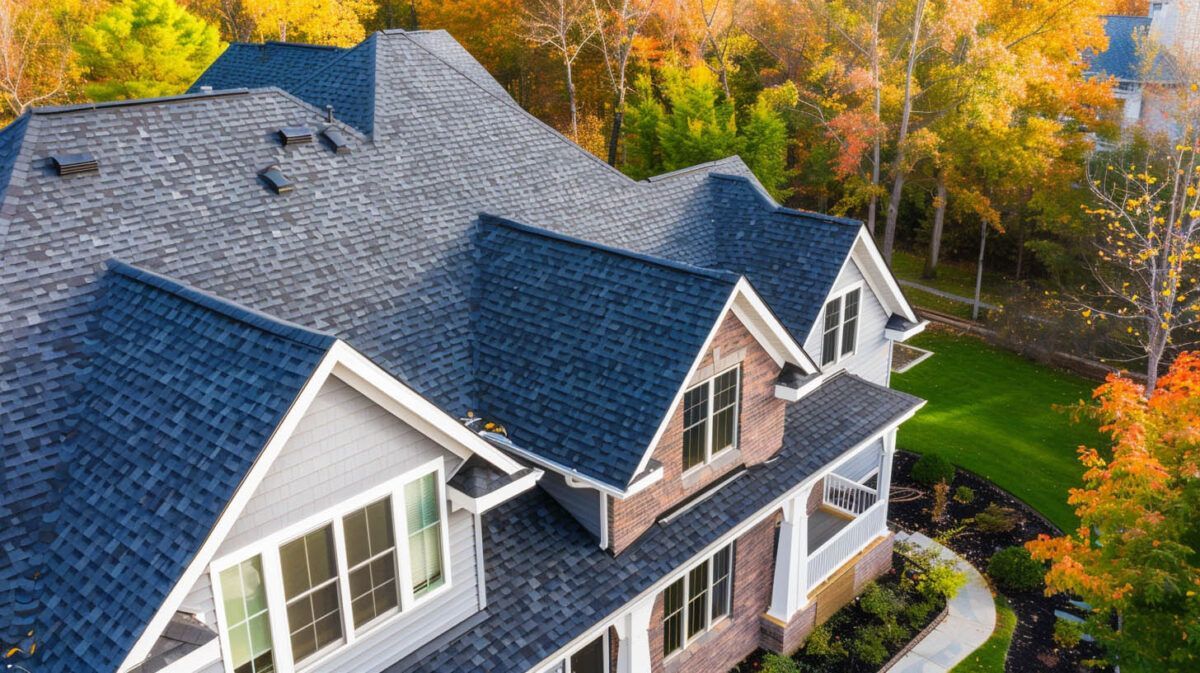 Aerial view of a house with gray roof and stone exterior, surrounded by autumn trees and a landscaped lawn