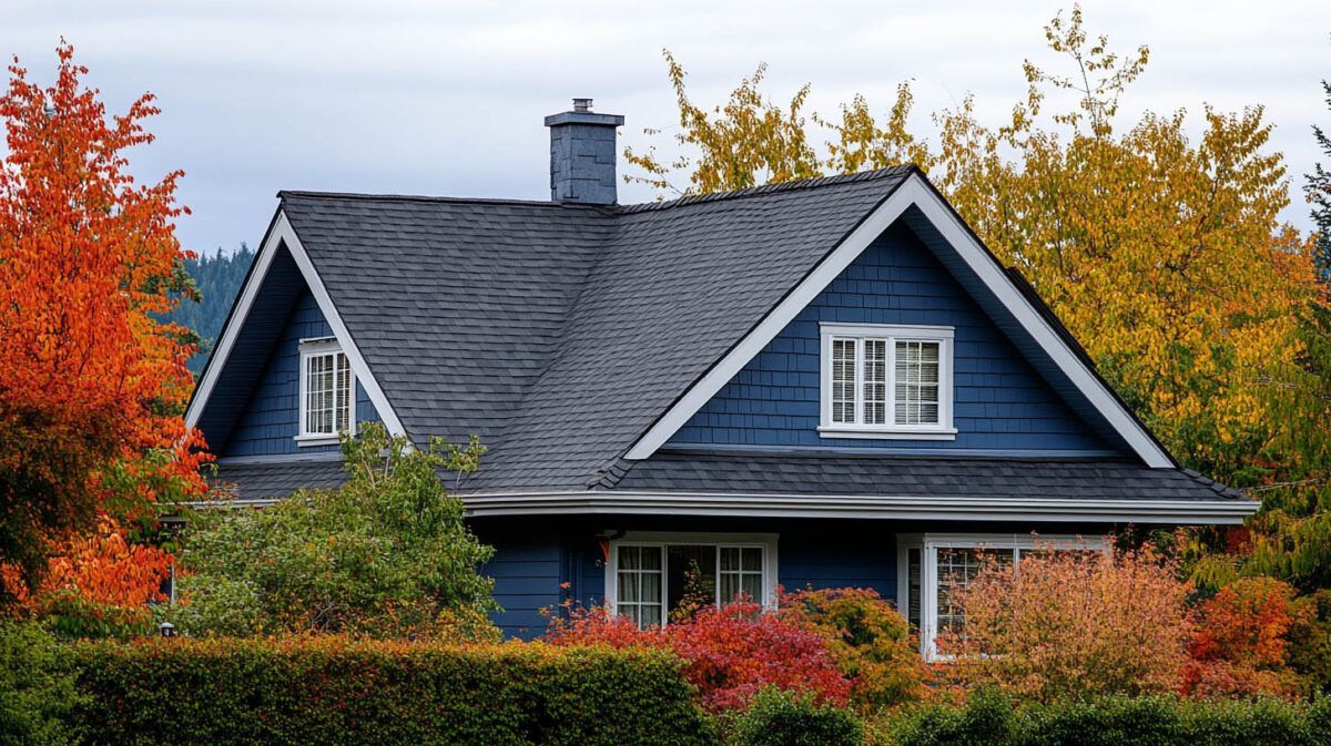 Blue house with a dark roof framed by colorful autumn trees and shrubs