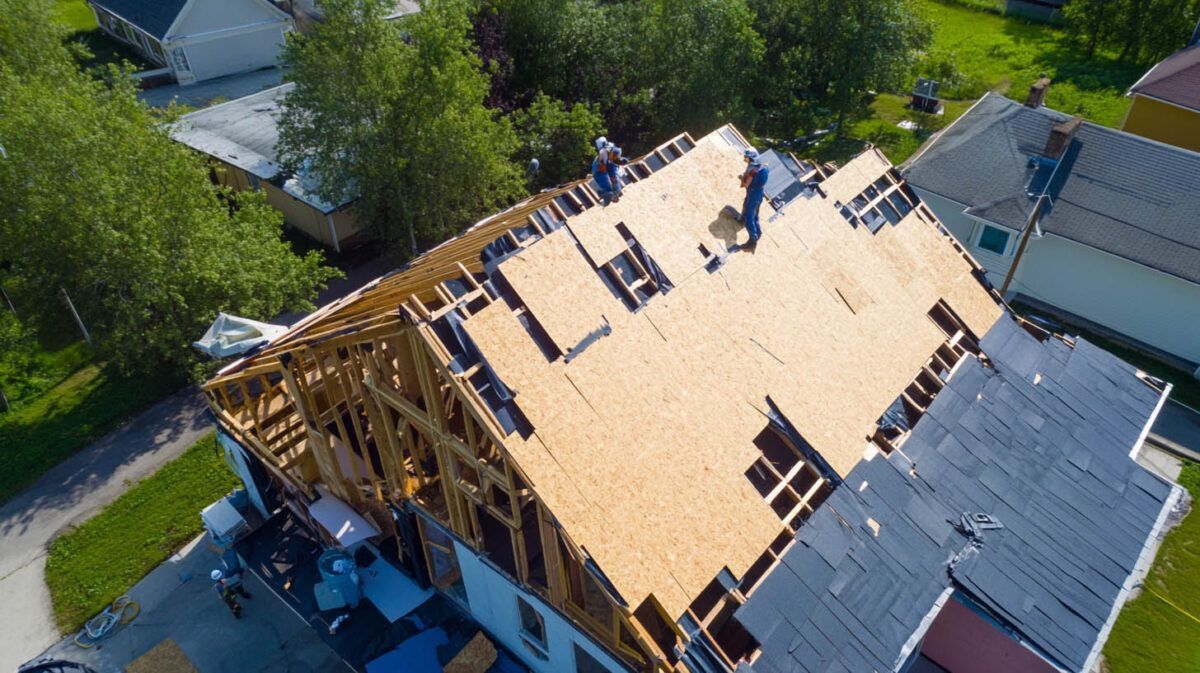 Aerial view of a house roof under construction with exposed wooden framing and unfinished sheathing