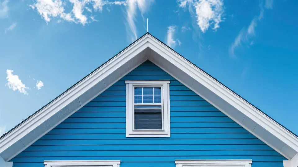 Blue house gable with white trim and a centered window against a bright sky