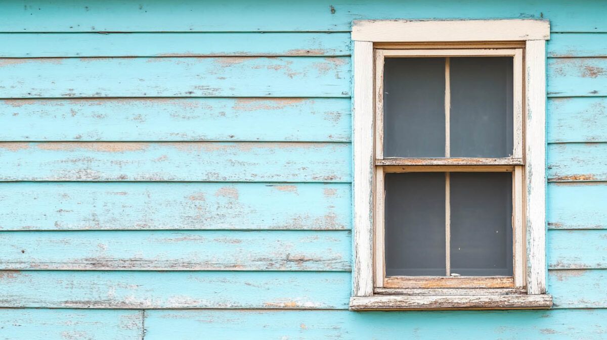 Weathered blue wooden siding with a small white-framed window.