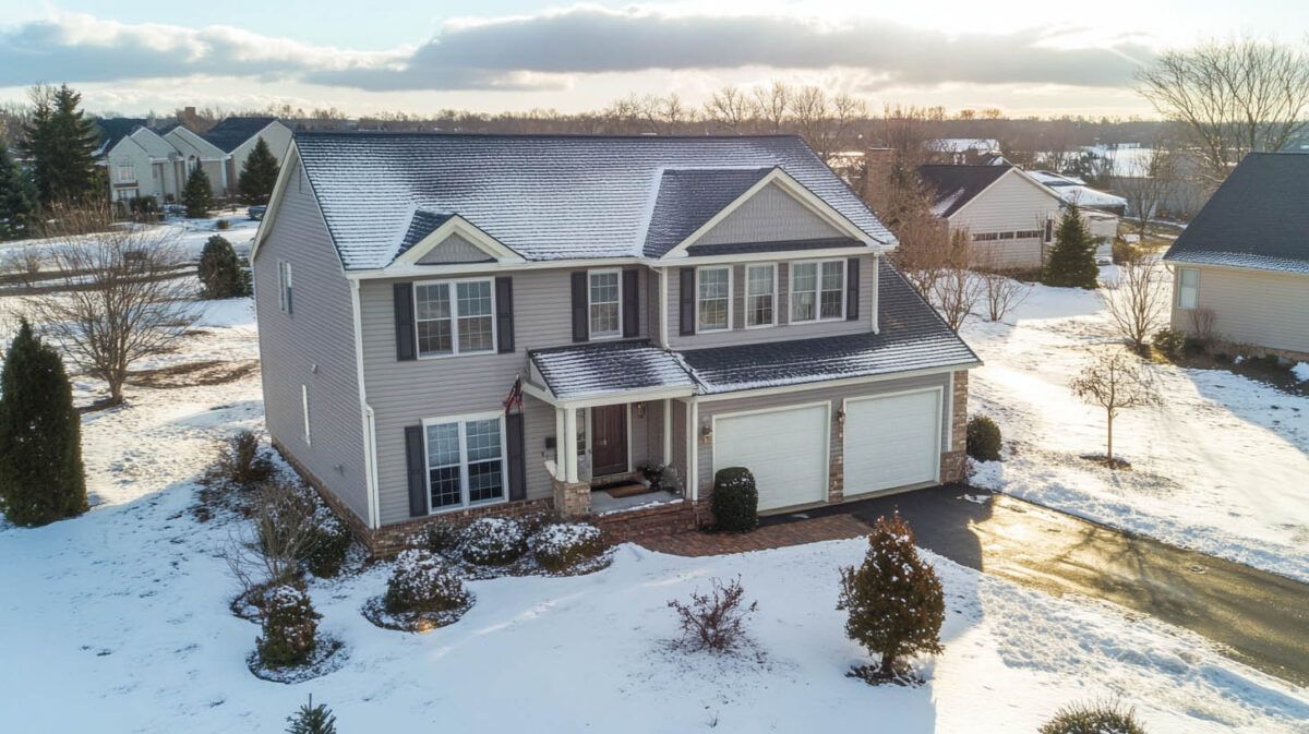 Snowy suburban house with gray siding and a covered porch in winter sunlight