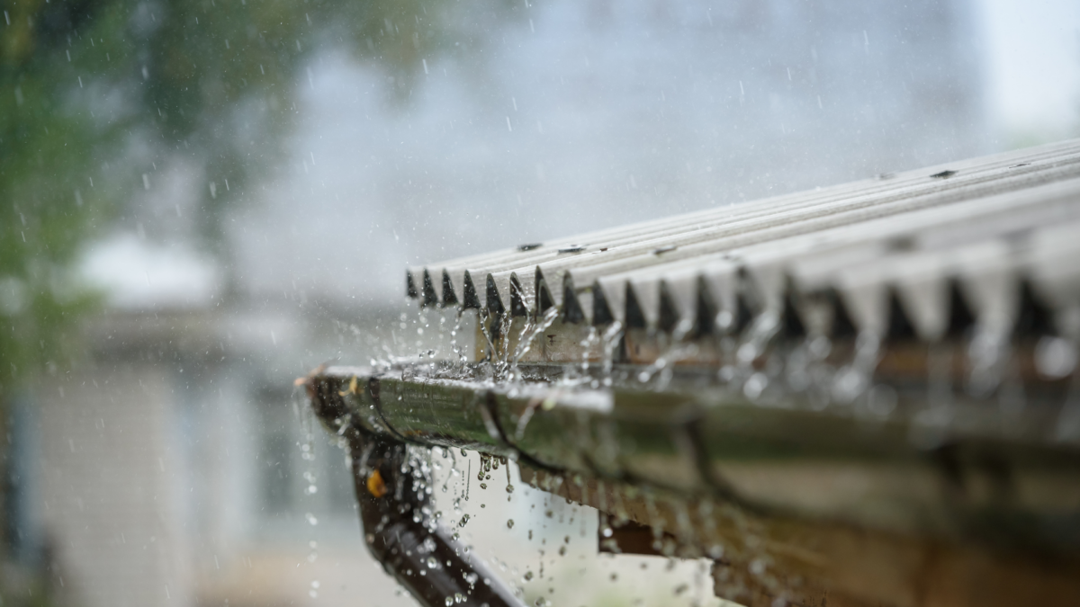 Rainwater dripping from a metal roof gutter during a downpour