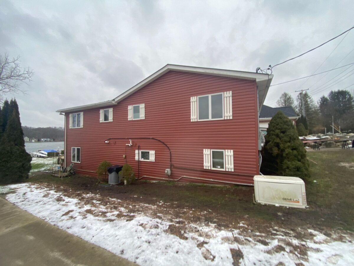 Red two-story house with white-trimmed windows on a snowy yard under an overcast sky