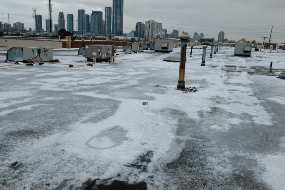 Snow-covered rooftop with city skyline in the distance under a gray sky