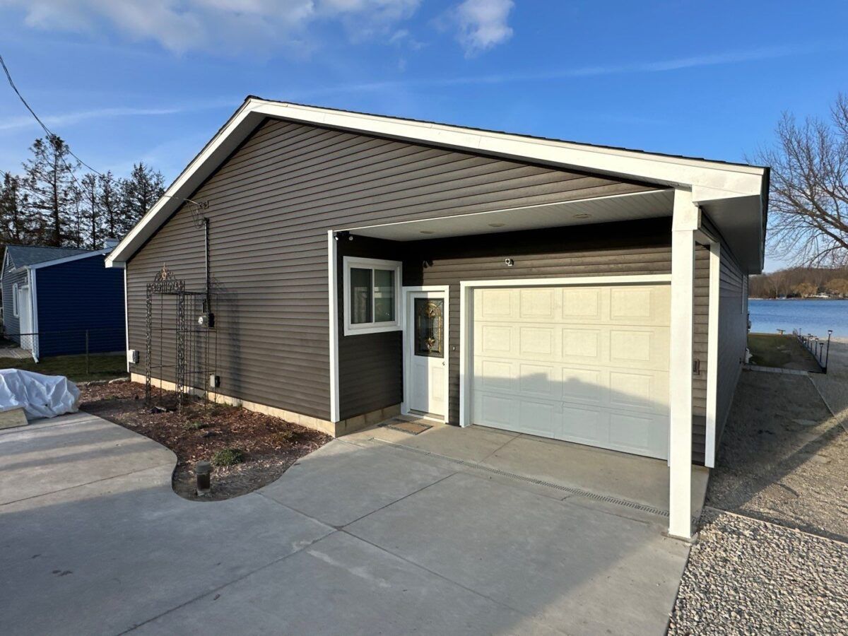 Small house exterior with attached garage, gray siding, and a concrete driveway under a blue sky