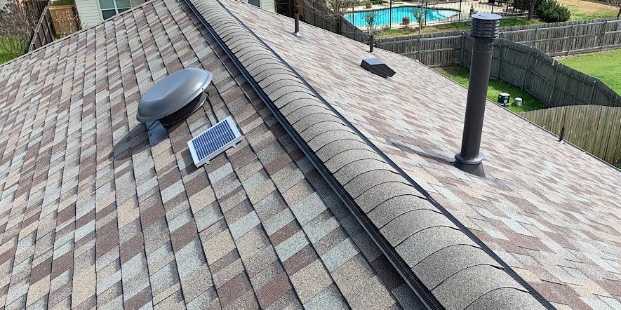 Rooftop with brown shingles, a skylight, and vent pipes under a clear sky