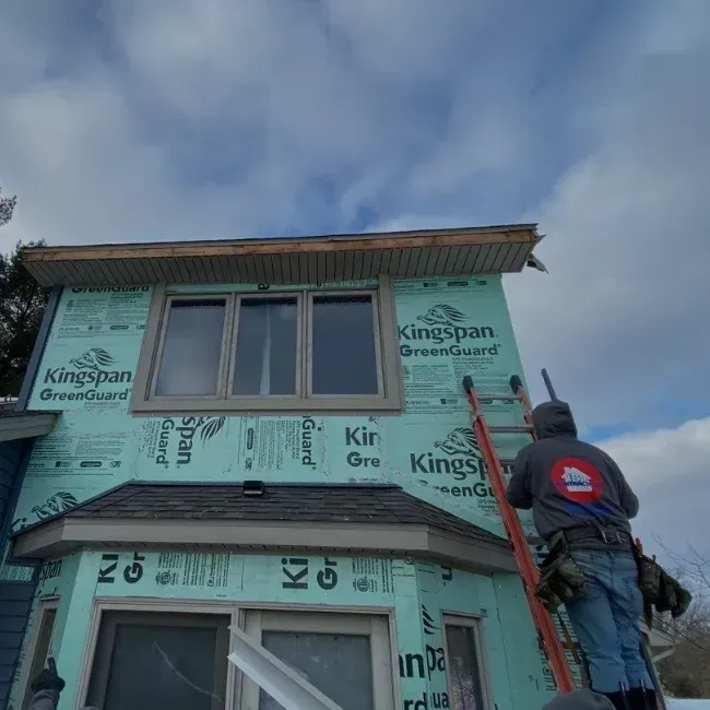 Worker on ladder installing green Kingspan insulated panels on a house exterior
