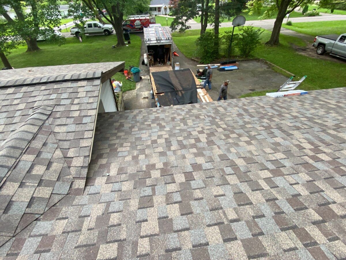 Roof view of a backyard with a driveway, truck, and workers near a dark rectangular pit