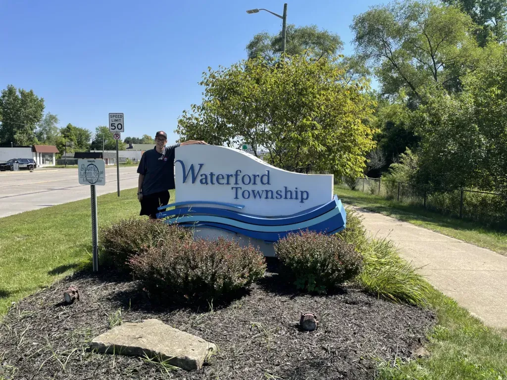 Waterford Township roadside sign in a landscaped area, with a person standing beside it.