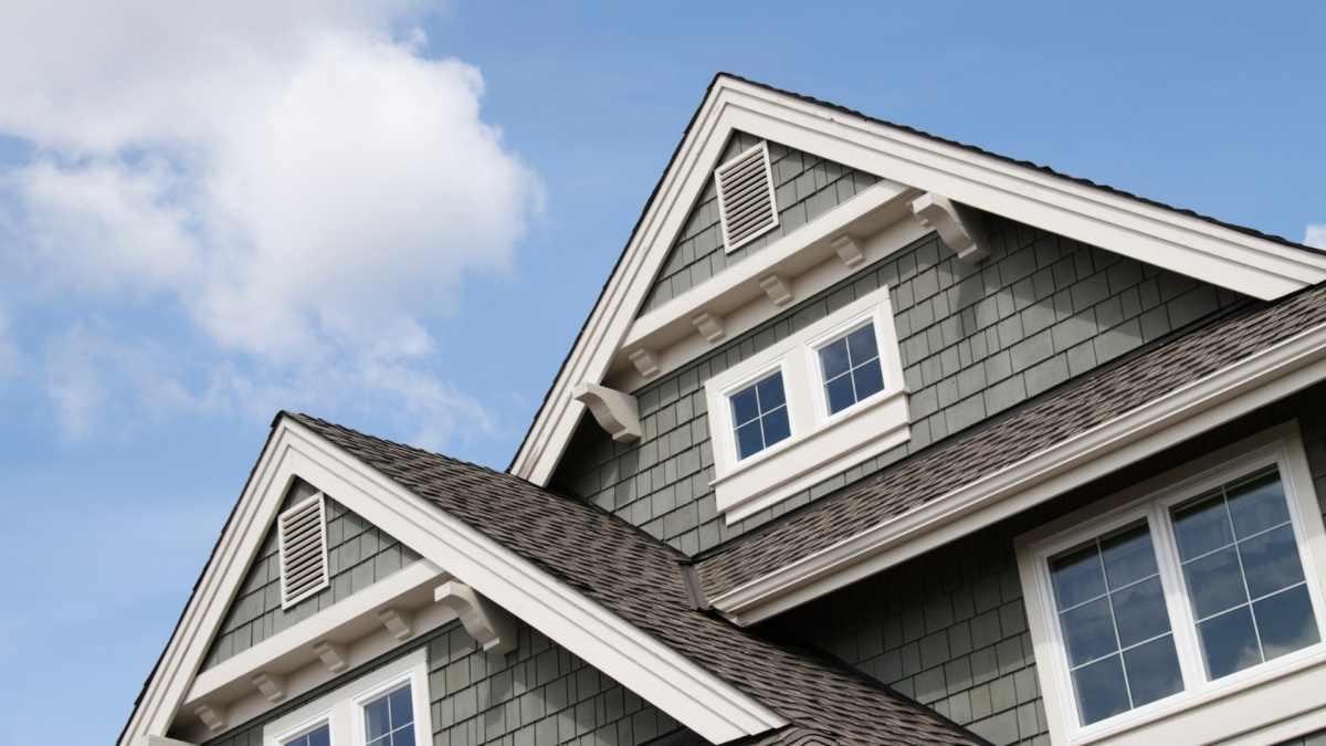 Two gray houses with white trim and dormer windows against a blue sky with clouds