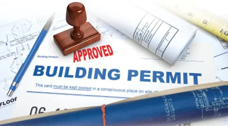 Approved building permit document with red stamp and blueprints in the background
