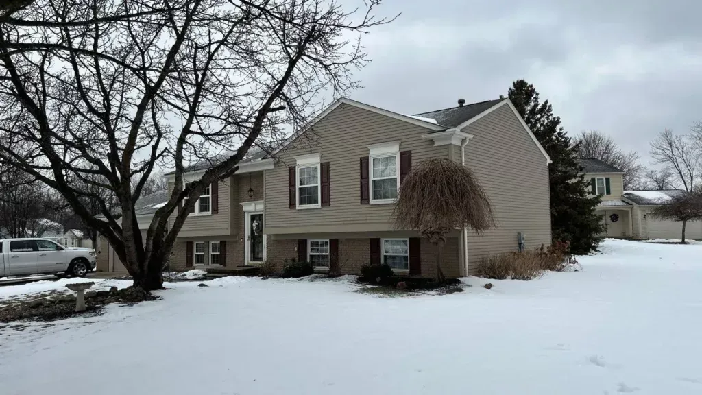 Snow-covered suburban house with bare trees and overcast winter sky