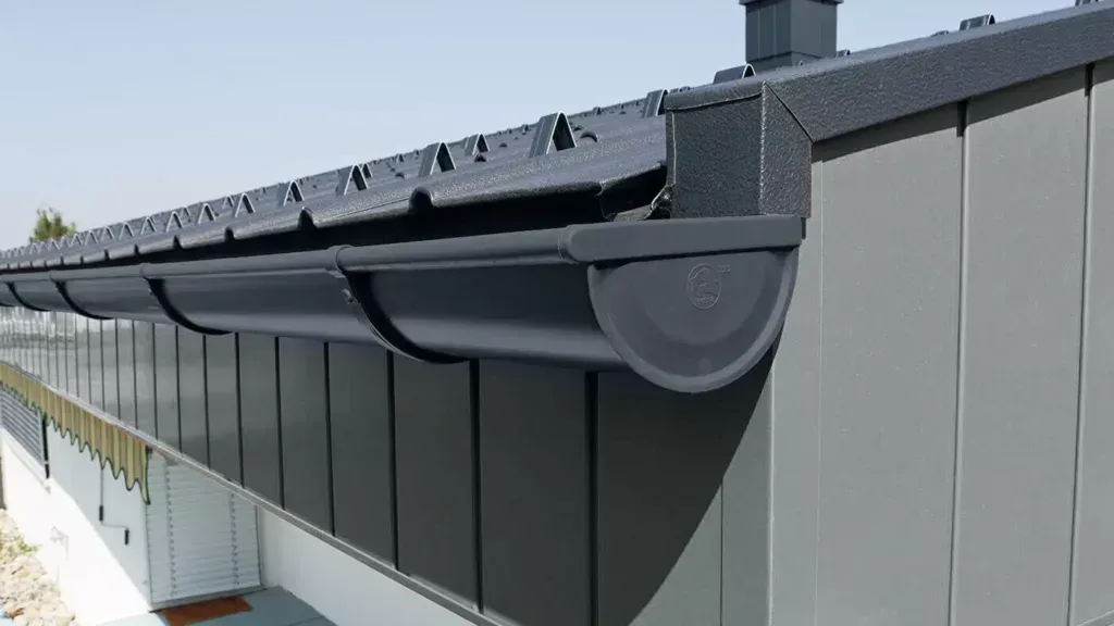 Black rain gutter and downspout on a gray building exterior under a sloped roof.