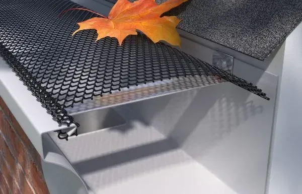 Black metal mesh gutter guard on a roof edge with an orange autumn leaf resting on top