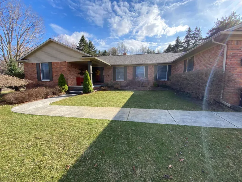 Single-story brick house with front lawn, concrete walkway, and bright blue sky