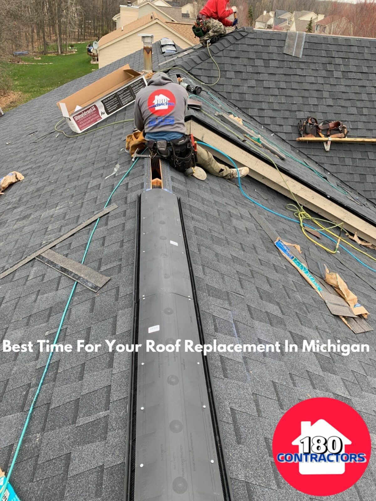 Roofers installing black shingles on a steep roof in Michigan, with one worker on the ridge.