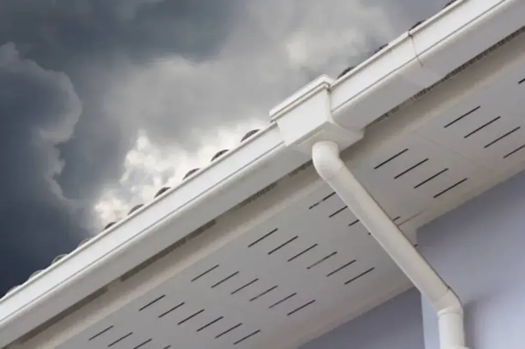 White house eaves and downspout against a cloudy gray sky