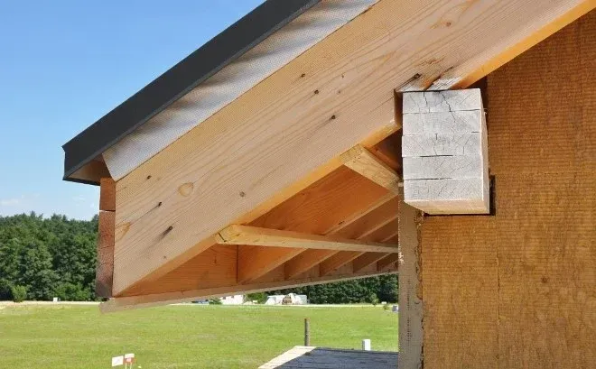 Close-up of a wooden building roof overhang with exposed rafters and a small vent box on the wall.