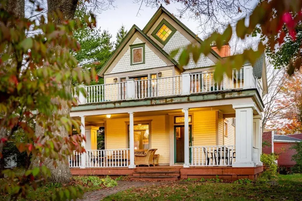 Victorian-style white house with a porch, gabled roof, and autumn trees in front