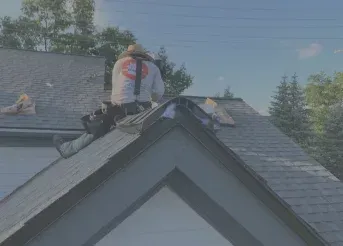 Person on a roof near a chimney, working on gray shingles under a clear sky