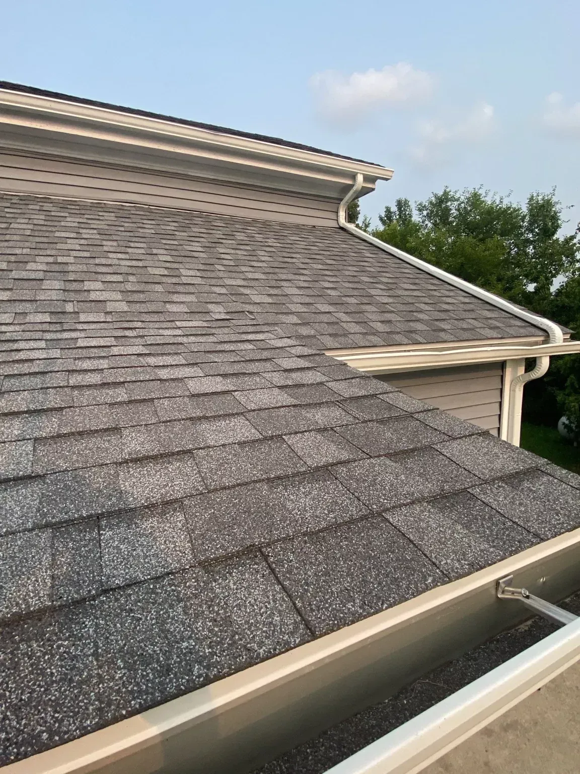 Gray shingled roof with white gutters under a blue sky, viewed from above