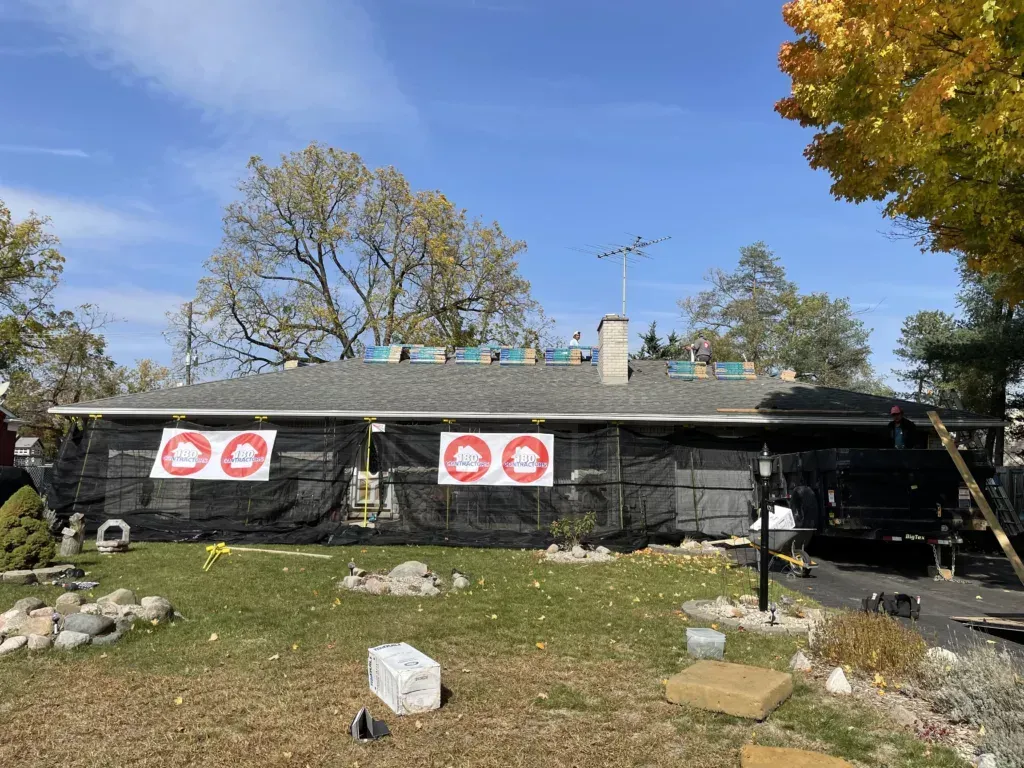 Black house with red warning signs and debris in yard under a blue sky