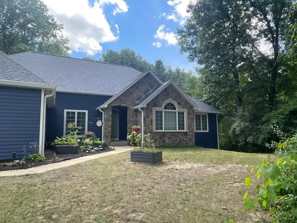 Suburban house with stone entry, blue siding, and a front lawn under a partly cloudy sky