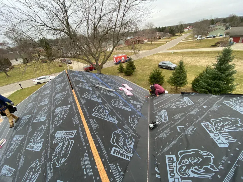 Two people writing messages on a large black roof surface in a suburban yard.