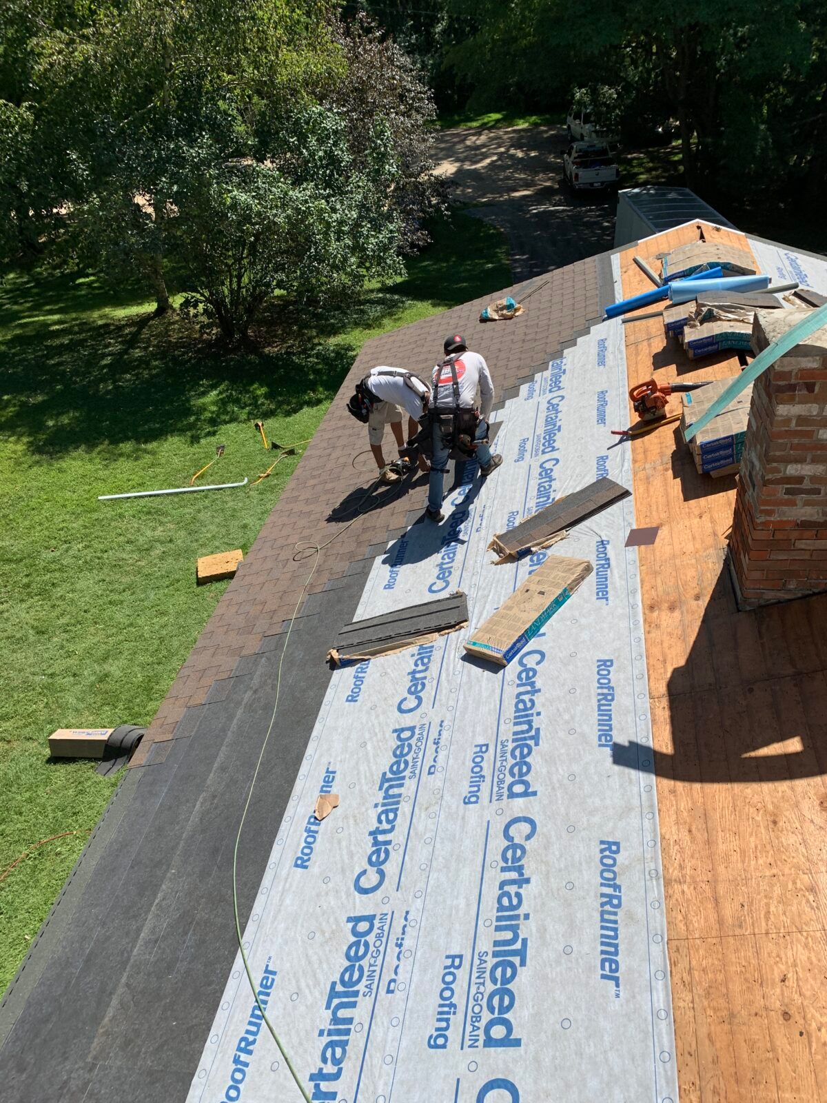 Workers installing roofing shingles on a house roof, with tools and underlayment visible.