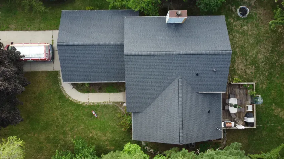 Aerial view of a gray-roofed house with a small patio and wooded yard around it