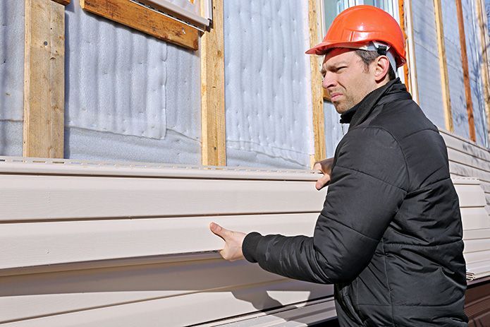 Worker in orange hard hat inspecting siding on a building exterior